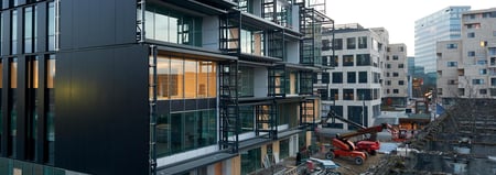 Byggeplass med moderne kontor- og boligbygg, kraner og maskiner - illustrasjon til artikkel om hvordan leverandører kan finne flere byggeprosjekter og anbud.